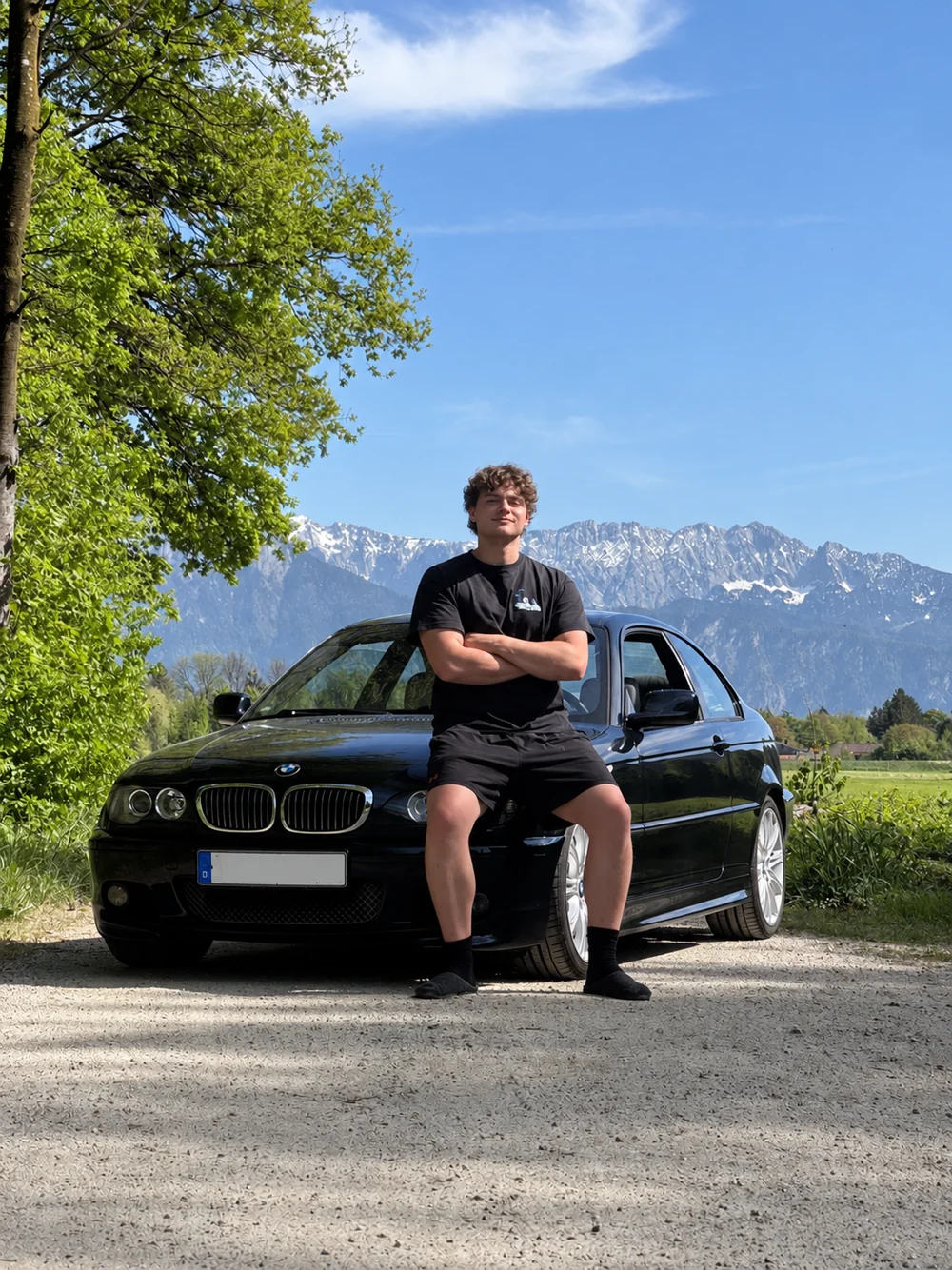 Maximilian Haak vor seinem schwarzen BMW E46 Coupé mit Alpenpanorama